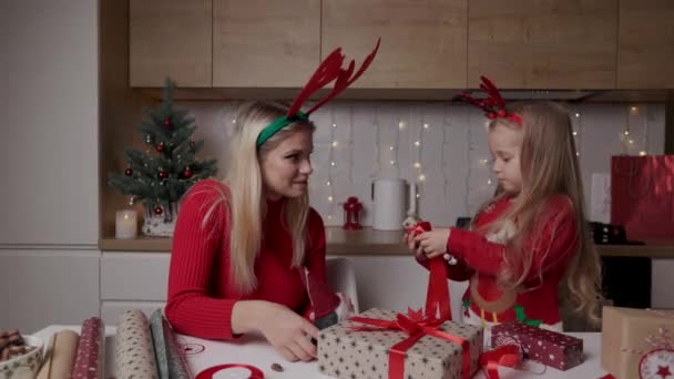 妈妈和女儿把圣诞礼物盒包装在装饰过的厨房后面 — 图库视频影像