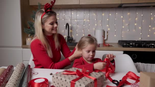 Mutter und Tochter wickeln Weihnachtsgeschenkboxen auf dem Hintergrund der dekorierten Küche — Stockvideo