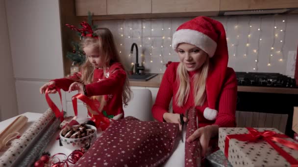 Mutter und Tochter wickeln Weihnachtsgeschenkboxen auf dem Hintergrund der dekorierten Küche — Stockvideo