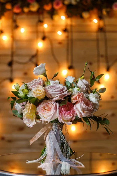 Delicate en zeer mooie bruiloft boeket van rozen, groen, eustoma staan op spiegel tafel. Bruids trendy bloemen in pastelkleuren op de achtergrond van de avondgloeilampen. — Stockfoto