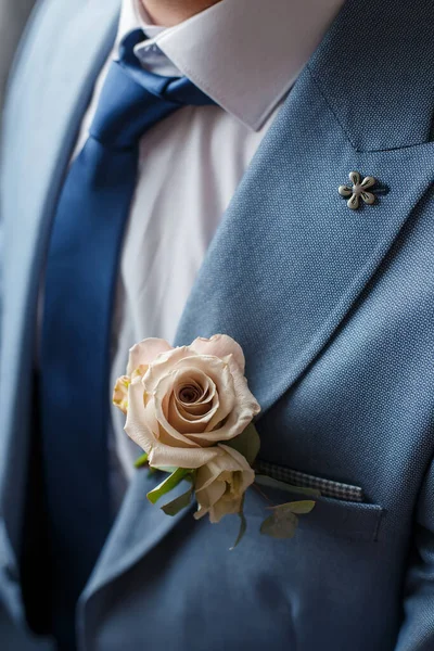 Boutonniere av beige ros blomma och grönska fäst vid den blå kostym brudgummen. Bröllopsdetaljer och blomsterhandel. — Stockfoto