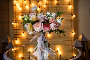 Nazik ve çok güzel bir buket gül, yeşillik, ayna masasında duran mutluluk. Akşam lambalarının arka planında pastel renkli gelinlik çiçekleri var..