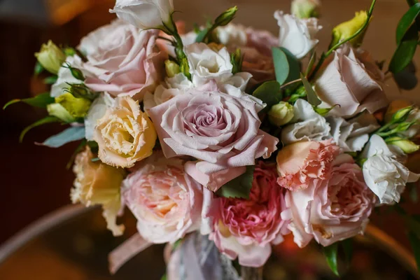 Нежный и очень красивый свадебный букет из роз, зелени, эустомы, стоящей на зеркальном столе. Свадебные модные цветы в пастельных тонах на фоне вечерних лампочек освещения. — стоковое фото