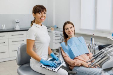 Diş muayenesi sırasında hastaya tedaviyi açıklayan tablet ve röntgen resimli arkadaş canlısı bir dişçi. Modern diş kliniği. Profesyonel ağız bakımı kavramı, stomatoloji ofisinde danışma