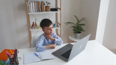 Evde ders çalışırken bilgisayarla öğretmenle konuşan bir çocuk. İlköğretim okulunu video aracılığıyla öğreniyorum. Akıllı çocuk internet ve alet kullanarak ev ödevi yapıyor..