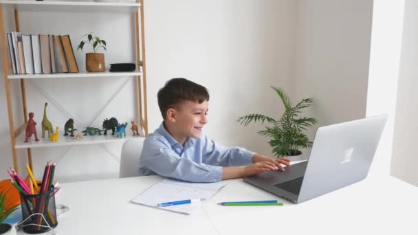 Dzieciak przez laptopa rozmawia z nauczycielem podczas nauki online w domu. Szkoła podstawowa e-learning za pomocą połączenia wideo. Zabawny chłopiec robi pracę domową za pomocą Internetu i gadżet. — Wideo stockowe