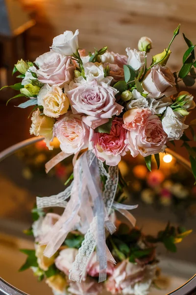 Λεπτή και πολύ όμορφη γαμήλια ανθοδέσμη από τριαντάφυλλα, πράσινο, ευστόμα στέκεται στο τραπέζι καθρέφτη. Νυφικά μοντέρνα λουλούδια σε παστέλ χρώματα στο φόντο των λαμπτήρων φωτισμού βράδυ. — Φωτογραφία Αρχείου
