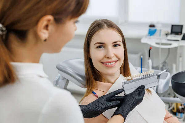 Dentysta zademonstruje pacjentom kolor zębów przewodnik do wybielania zębów. Kolor zębów pasujące próbki do implantów lub oklein w rękach lekarza. Zdjęcie koncepcyjne na temat stomatologii — Zdjęcie stockowe