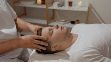 Genç adam, SPA salonundaki profesyonel kafa masajı sırasında dinleniyor. Elle migren tedavisi. Sağlık, vücut ve sağlık hizmetleri kavramı