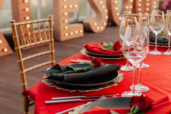 客人餐桌设置为黑色,红色和金色风格的宴会.精致的晚餐：装饰、桌布、餐巾纸盘、新鲜玫瑰、眼镜、餐具。屋顶上的派对庆祝活动，户外. — 图库照片