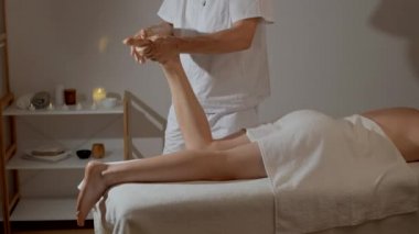 Mumların arka planında SPA salonunda profesyonel bacak masajı. Beyaz üniformalı yakışıklı masör atlet kasları için manüel terapi yapıyor. Sağlık, vücut ve sağlık hizmetleri kavramı