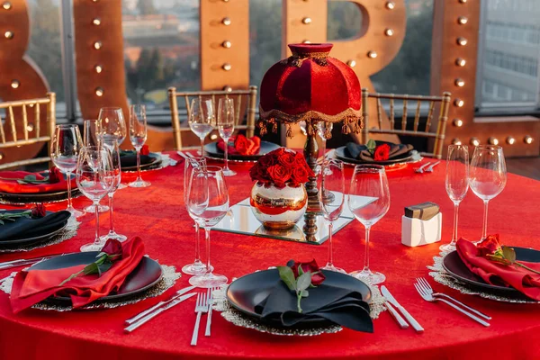 客人餐桌设置为黑色 红色和金色风格的宴会 精致的晚餐 餐巾纸盘 新鲜玫瑰 屋顶上的派对庆祝活动 — 图库照片