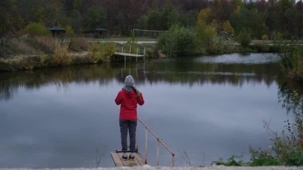 Редкий вид женщины стоит на пирсе. осень. озеро — стоковое видео