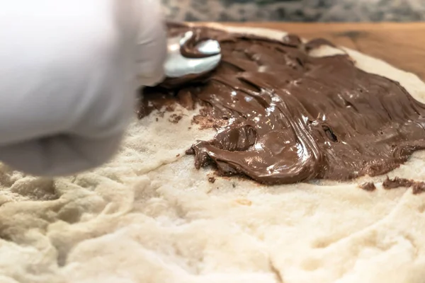 Chocolate pizza on wooden board. Sweet pizza. A hand with white gloves topping the pizza with chocolate cream.