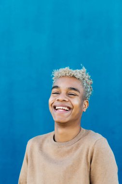 Mavi arka planda gülümseyen genç Latin Amerikalı bir erkeğin portresi.