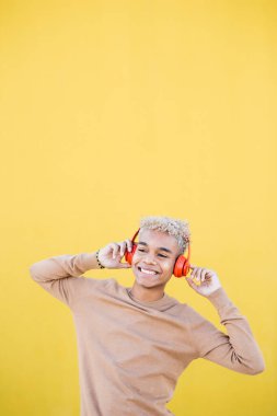 Kırmızı kulaklık takan ve sarı arka planda dans eden gülümseyen genç adamın portresi.