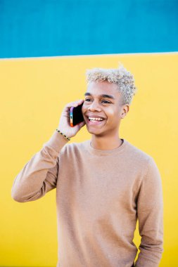 Genç Latin Amerikalı erkek mavi arka planda akıllı telefon kullanıyor.