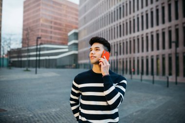 Genç gülümseyen bir adam kırmızı bir telefondan yürüyor ve konuşuyor.