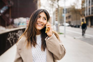 Sokakta telefonla konuşan gülümseyen bir kadının portresi.