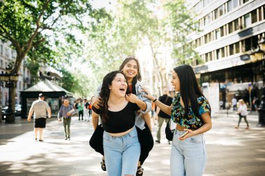 Barselona 'nın Las Ramblas' ında yürürken bir arkadaşını sırtında taşıyan genç kadınlar