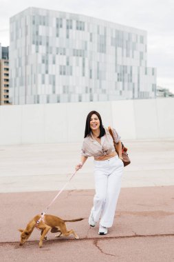 Genç bir kadın köpeğiyle sokakta yürüyor.