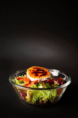 Green salad with cheese on top in a big bowl over a black backgroun