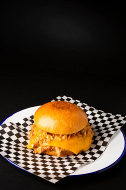 Pulled chicken burger with cheese over a black background