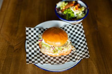Chicken burger with cheese accompanied with green salad on a white plate on a wooden table 