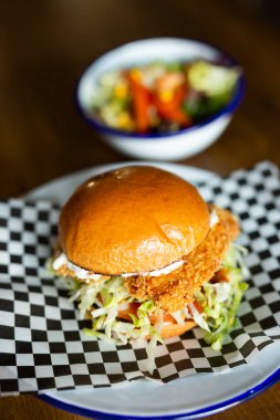 Finger Chicken burger with cheese accompanied with green salad on a white plate on a wooden table
