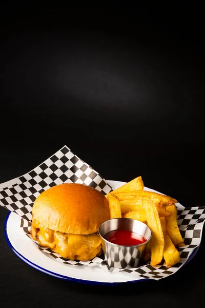 Two smashed hamburgers with cheese accompanied with french fries on a white plate over a black background