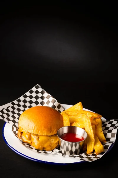 Two smashed hamburgers with cheese accompanied with french fries on a white plate over a black background 