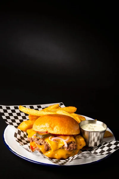 Two smashed hamburgers with cheese accompanied with french fries on a white plate over a black background
