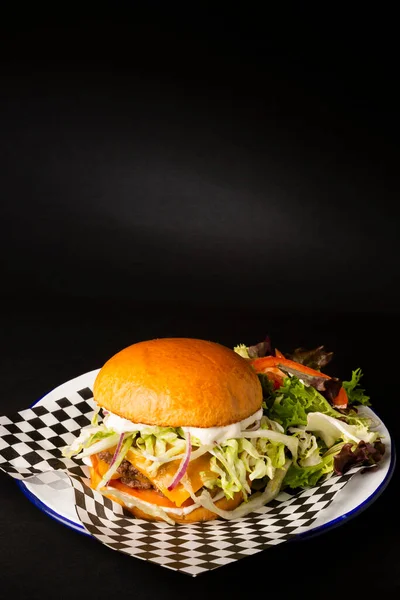 Two smashed hamburgers with cheese accompanied with a green salad on a white plate over a black background
