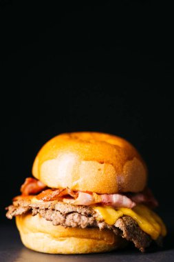 Doble cheeseburger with bacon, melted cheese and ketchup over a black background