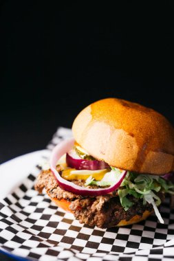Doble cheeseburger with vegetables on a white plate over a black background