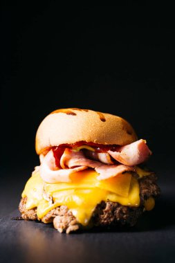 Doble cheeseburger with bacon, melted cheese and ketchup over a black background