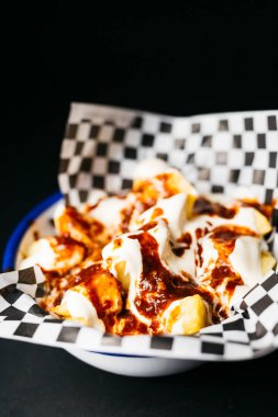 Fried potatoes with mayonnaise and tomato spacy sauce in a white plate over a black background