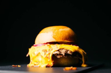 Doble burger with melted cheese topped with bacon over a black background