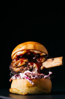 Beef rib burger and it's bone on a white plate on a wooden table over a black background