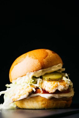 Chicken burger with vegetables over a black background
