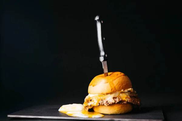 Doble smashburger with coocked onion and a boiled egg over a black background
