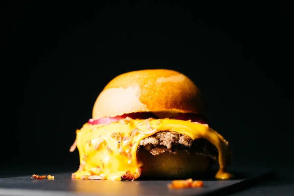 Doble burger with melted cheese topped with bacon over a black background