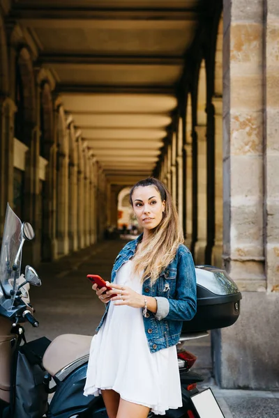 Kırmızı akıllı telefon kullanan motosikletli genç bir kadın.