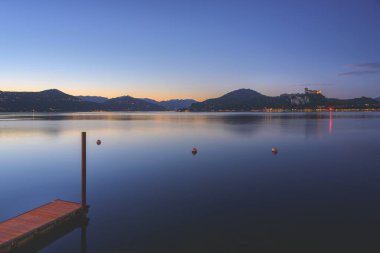 Arona, İtalya. Maggiore Gölü 'nde gün batımından sonra Arona köyünden panoramik manzara. Karşı kıyıda eski bir ortaçağ kalesi olan Rocca Angera 'yı görebilirsiniz. 10 Haziran 2022.