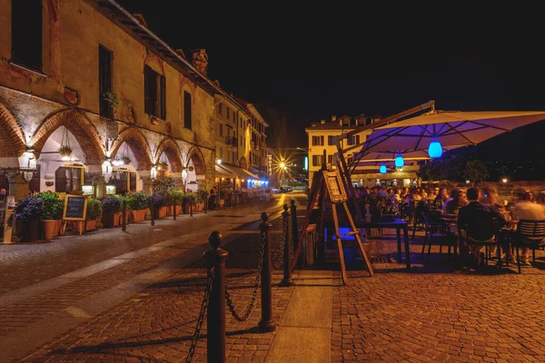 Arona, İtalya. Piazza del Popolo 'nun gece manzarası. İnsanlar bir restoranın dışında yemek yiyor. 10 Haziran 2022.