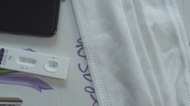 SARS-CoV-2 Antijen Rapid Test kitinin video taraması pozitif sonuç verdi, koruyucu maskeler, kulaklıklar ve bir takım anahtarlar yakınında bir masada.