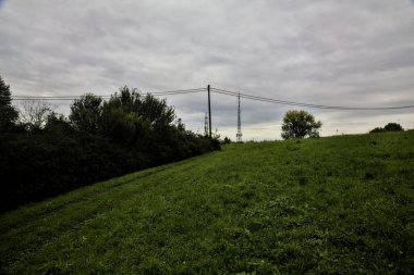 İtalya 'nın kırsal kesimlerinde bulutlu bir günde başlarının üzerinde kablolar olan bir tarlada çimenli bir yol.