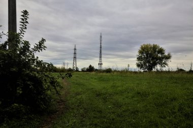 İtalya 'nın kırsal kesimlerinde bulutlu bir günde başlarının üzerinde kablolar olan bir tarlada çimenli bir yol.