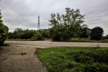 Arka planda bir korulukta bir antenle yol ve toprak yol arasında kırsal kesişiyor.