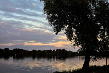 Sonbaharda ağaçlarla çevrili bir gölün üzerinde gün batımı